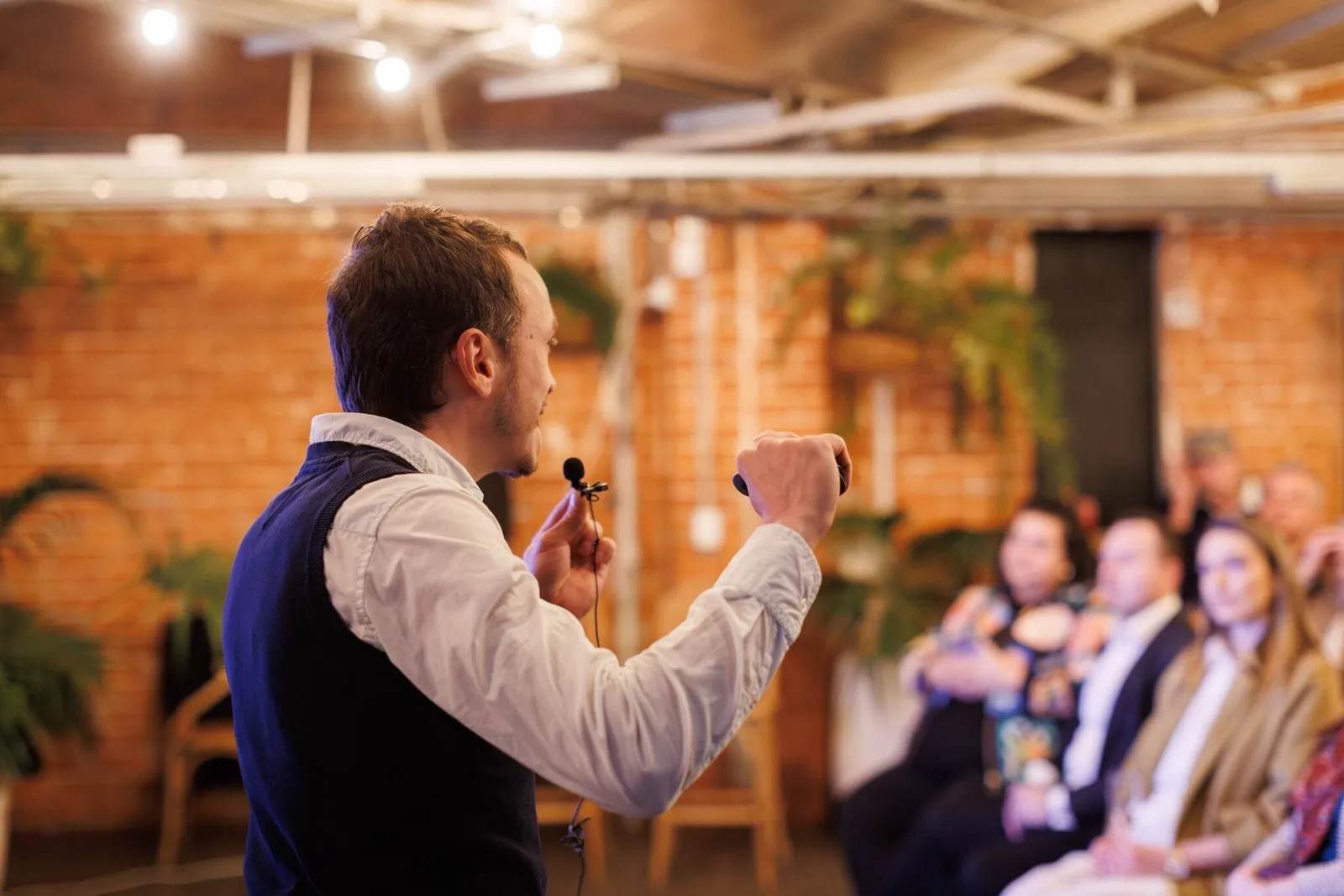Chris Lourenco presenting an AI workshop in Adelaide, speaking with a lapel microphone to a seated audience in a brick walled venue